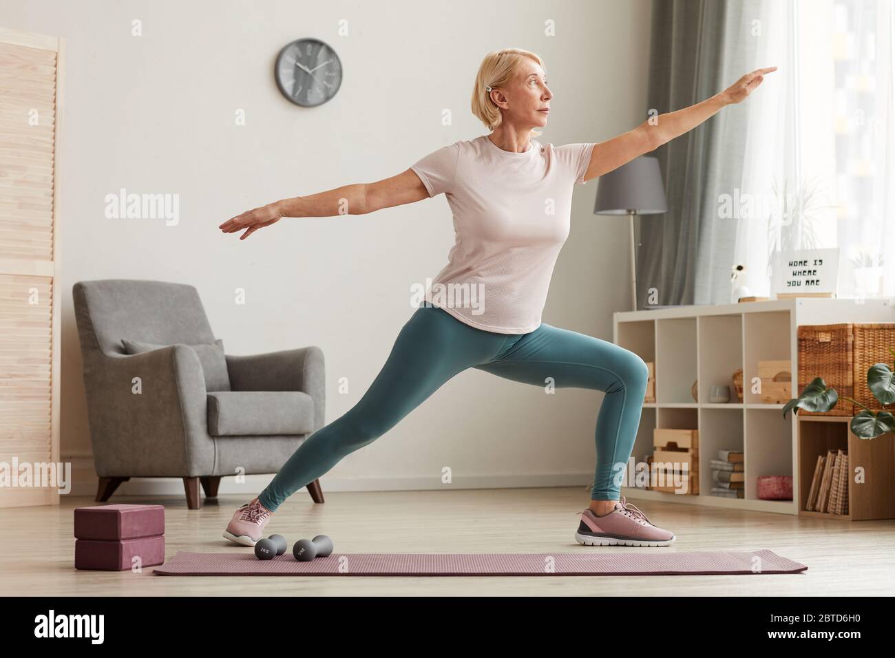 Mature woman standing on exercise mat and doing yoga in the living room at  home Stock Photo - Alamy