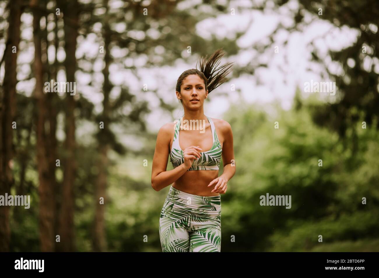 Pretty young fitness woman running at the forest trail Stock Photo