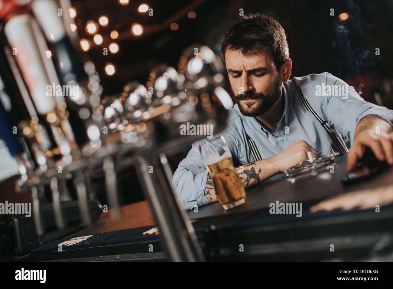 Young man drinking beer and smoking cigarette at pub in the night club Stock Photo