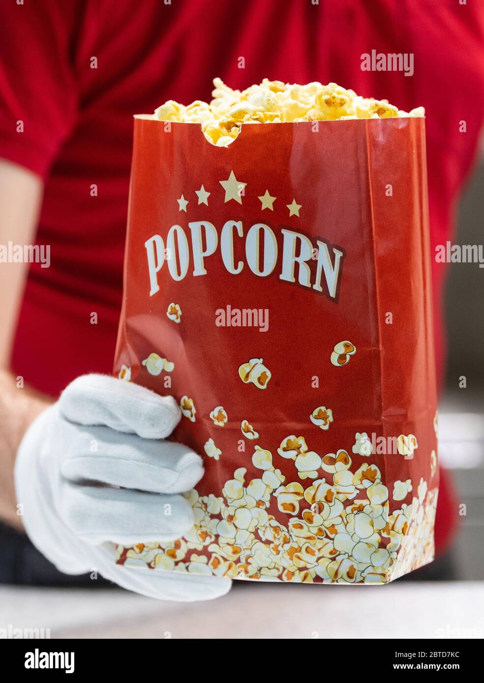 Dresden, Germany. 22nd May, 2020. An employee of the Ufa-Kristallpalast cinema in the Innnenstadt holds popcorn in his hands at the counter, wearing protective gloves. As the first big cinema in the city, the Ufa-Palast was allowed to reopen after the Corona lockdown. (to dpa 'With popcorn, without mask: How can a visit to the cinema look like now?') Credit: Robert Michael/dpa-Zentralbild/dpa/Alamy Live News Stock Photo