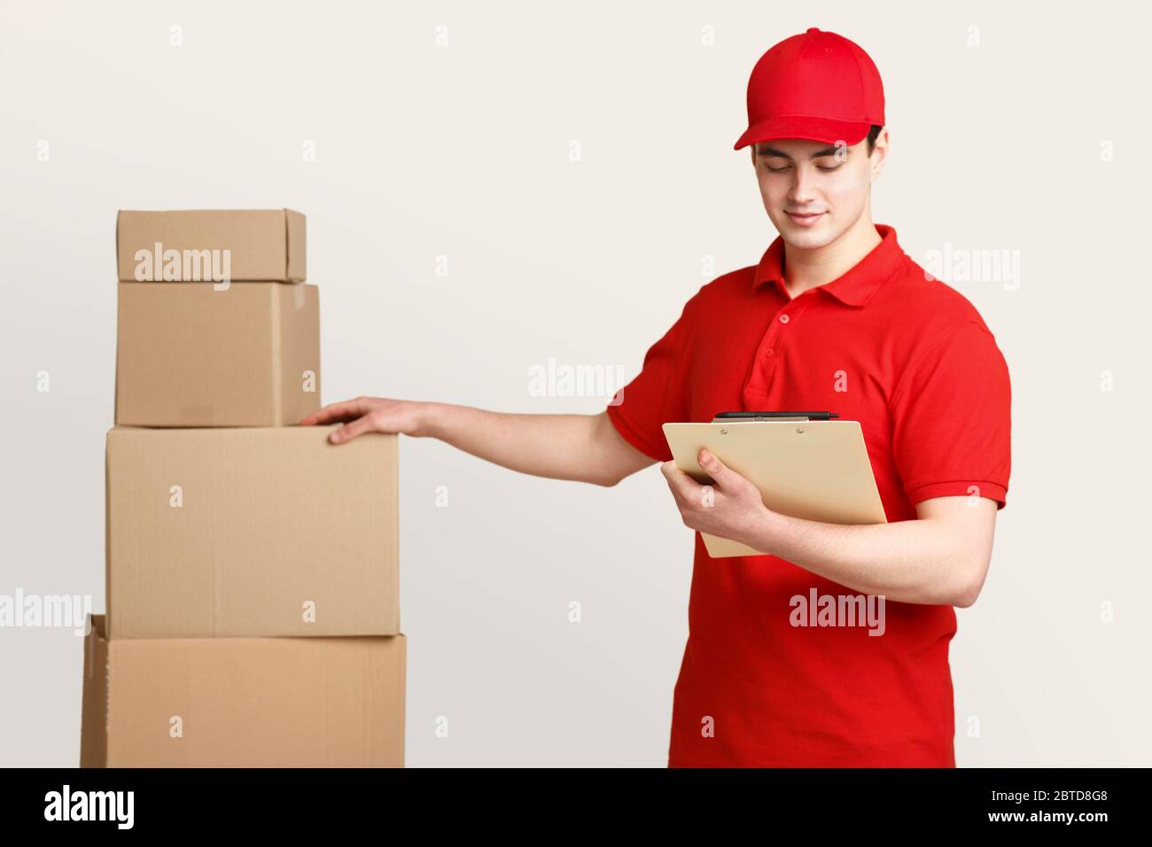 Postman in uniform at warehouse checks for presence of all parcels, holding tablet in hands Stock Photo