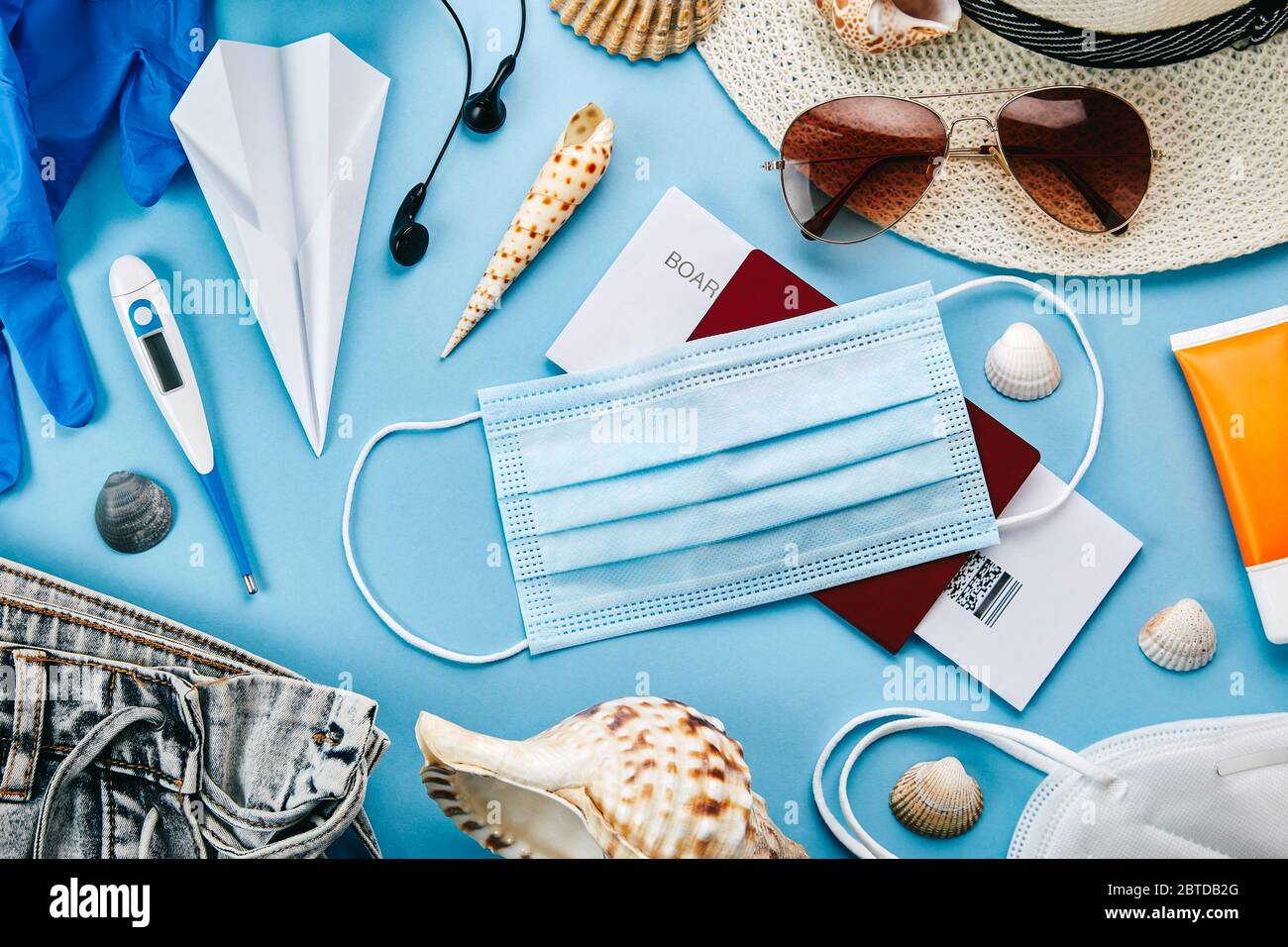 Overhead view of coronavirus travel accessories on blue background. Essential summer vacation items during the coronavirus pandemic. Covid-19 and trav Stock Photo