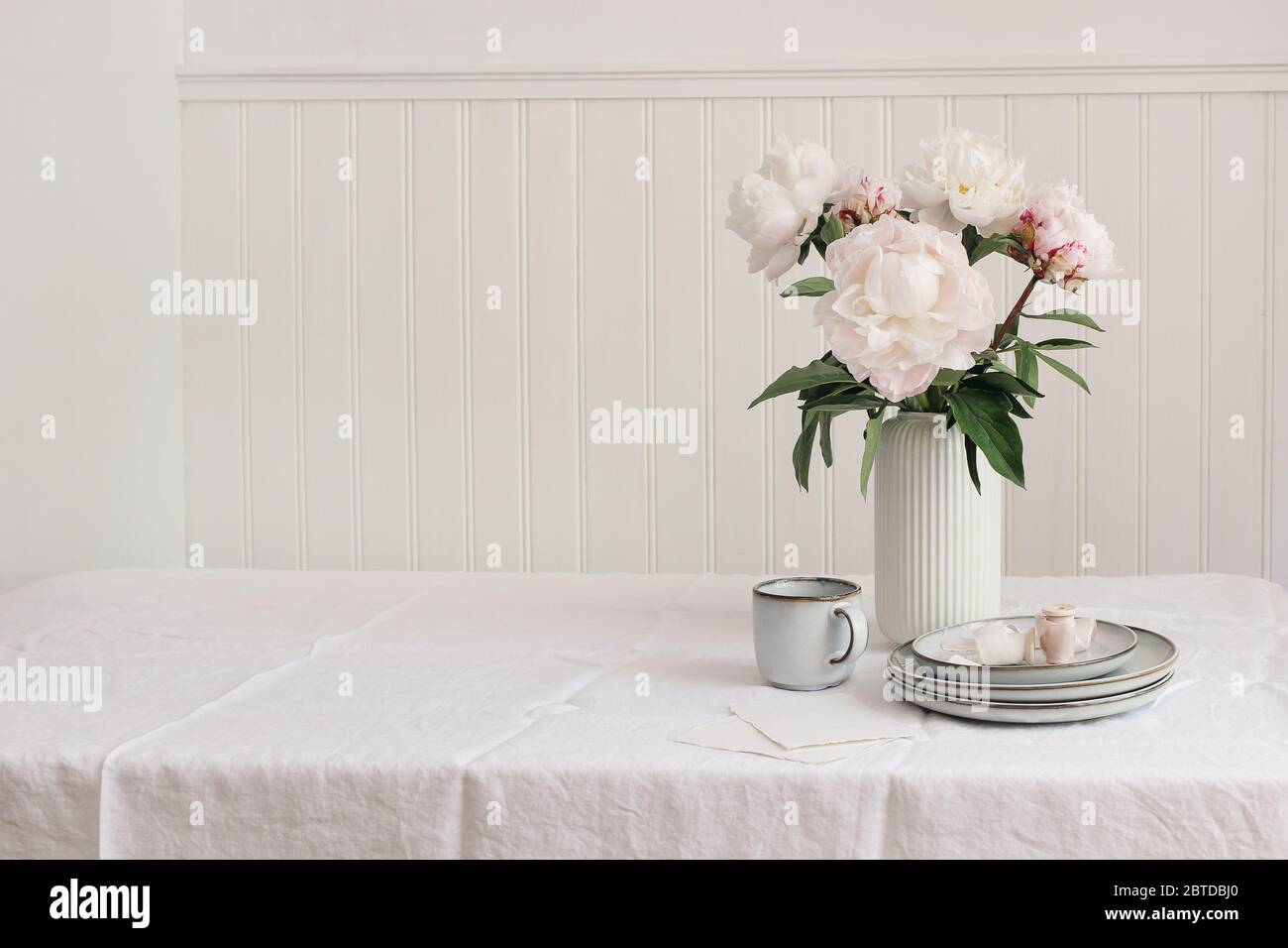 Styled stock photo. Feminine wedding or birthday table composition with floral bouquet. Pink peonies flowers, cup of coffee, plates and silk ribbons, Stock Photo
