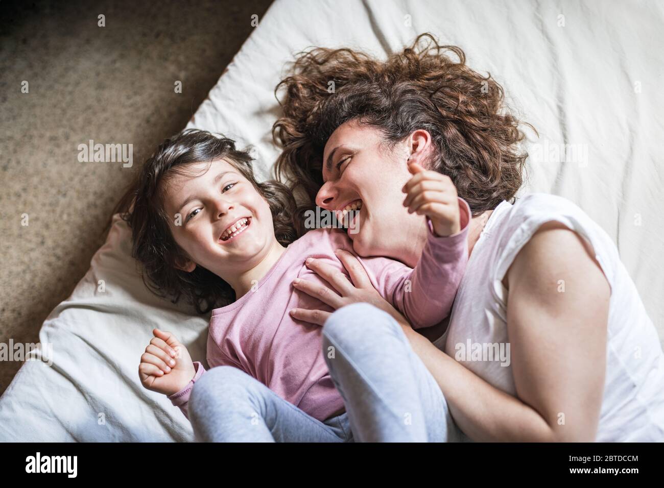 A mother tickles her daughter and laughs out loud while playing on the bed Stock Photo