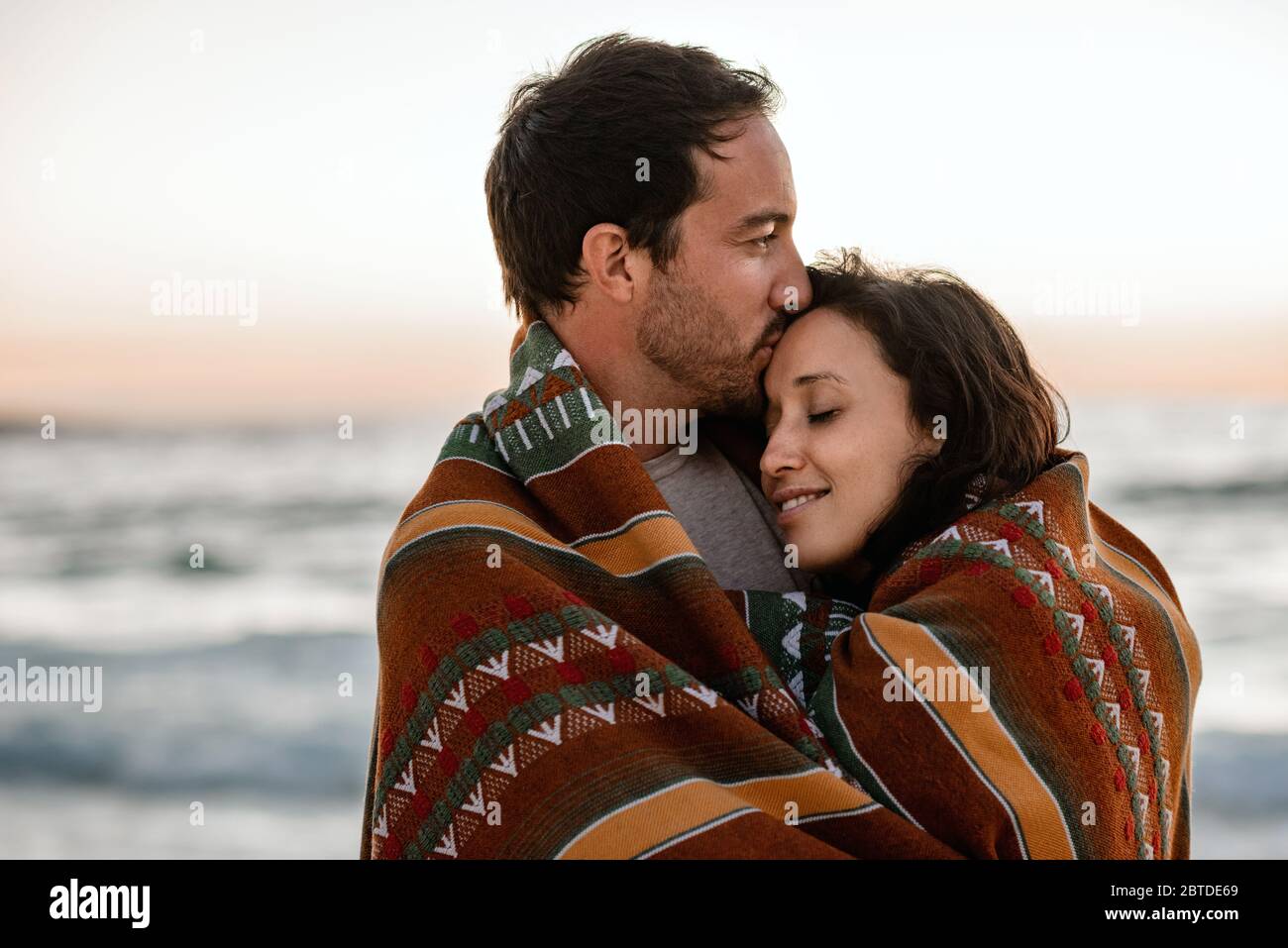 Loving couple standing on a beach wrapped in a blanket Stock Photo