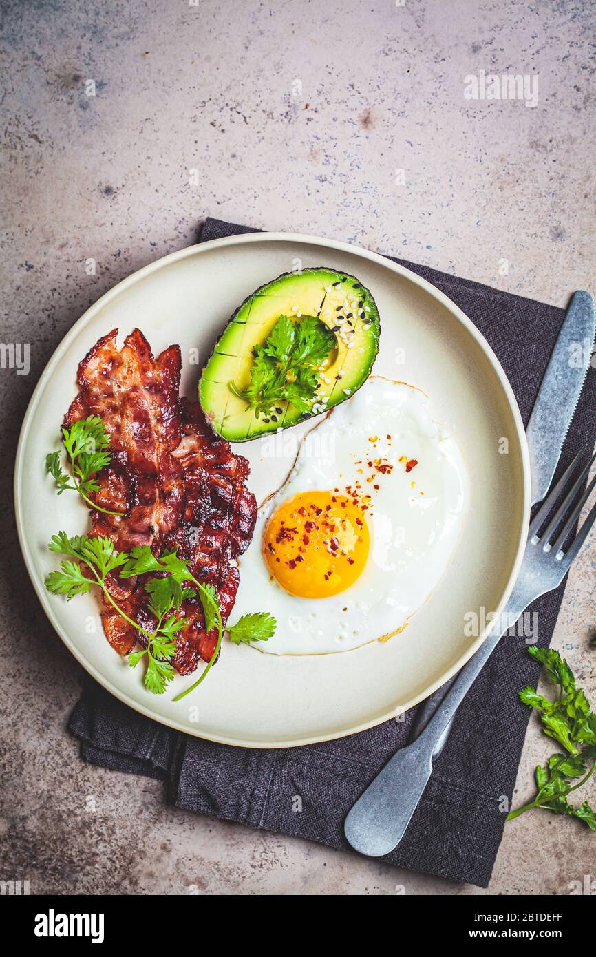 Keto breakfast - fried egg, avocado and bacon in a white plate. Keto diet concept. Stock Photo