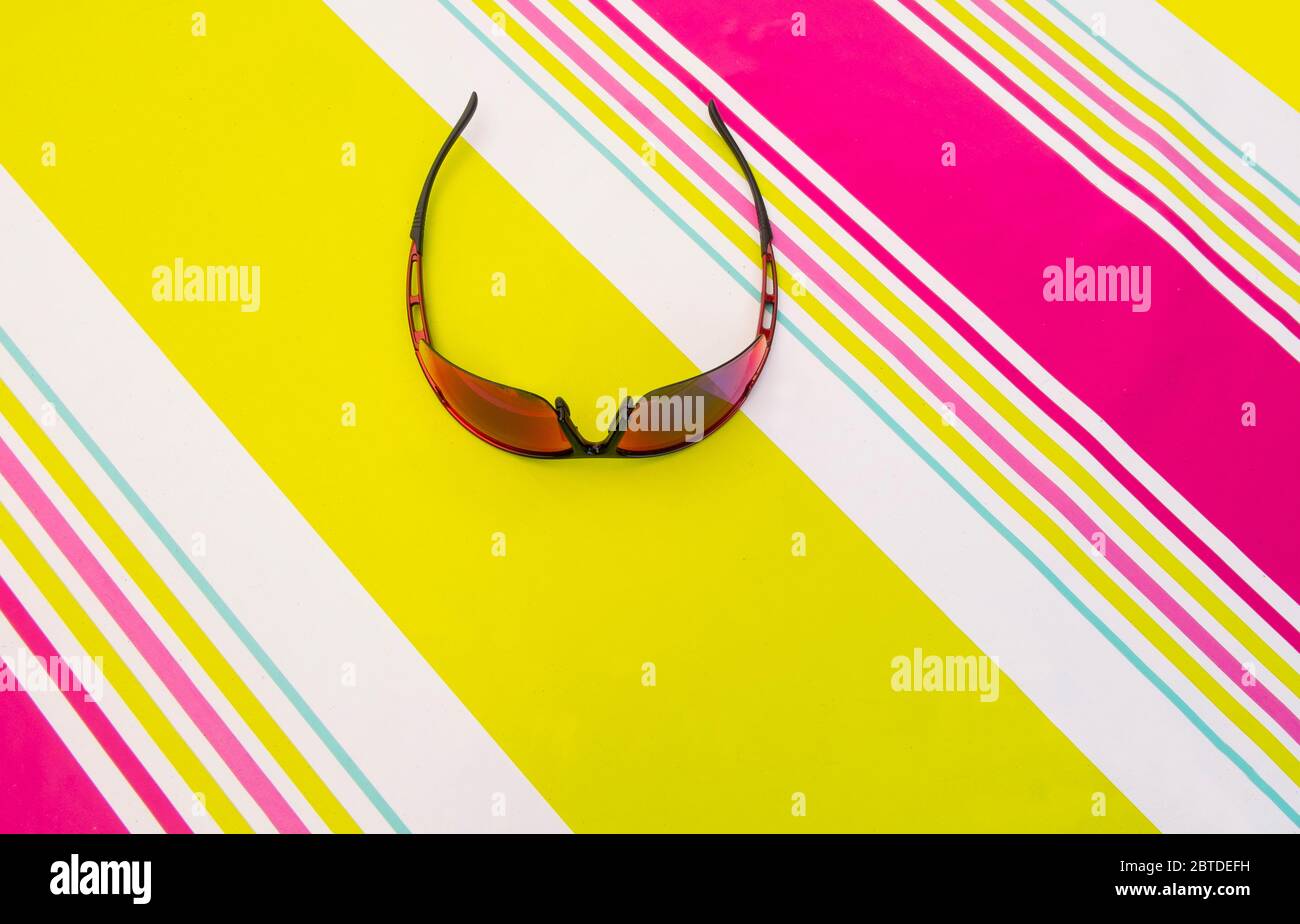 Sunglasses lying on a colourful striped tablecloth, overhead view Stock Photo