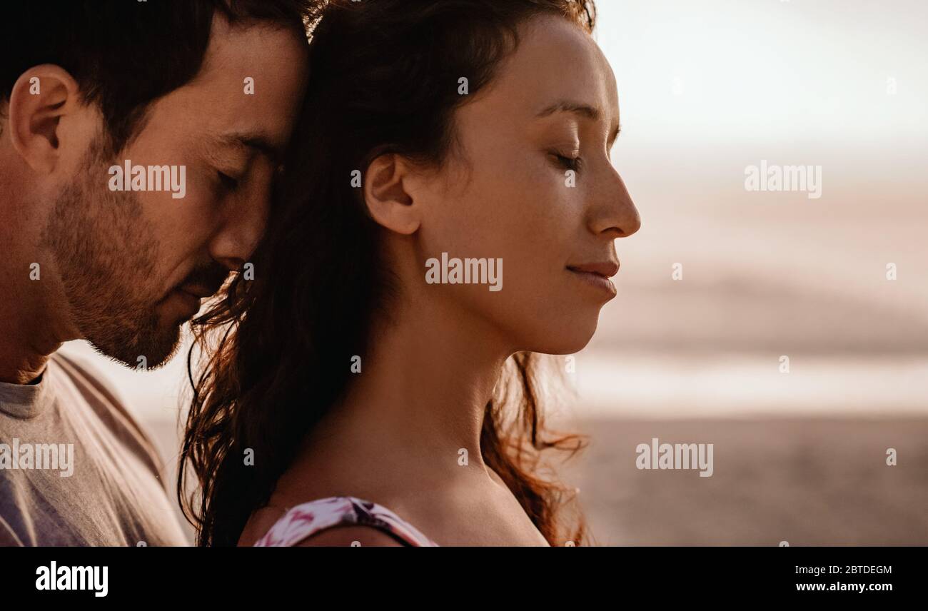 Loving couple standing close together on a beach at dusk Stock Photo