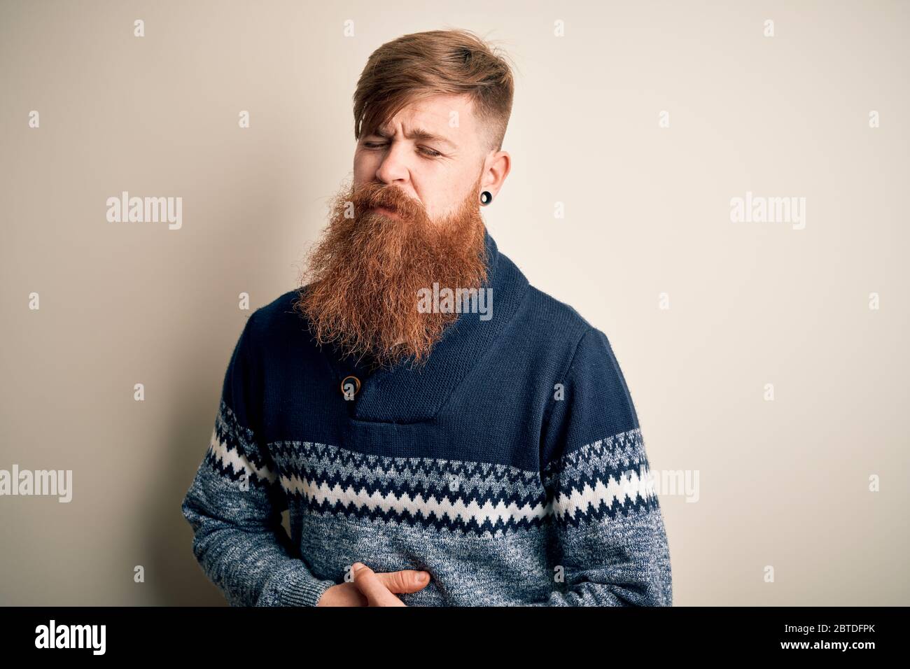 Handsome Irish redhead man with beard wearing winter sweater over isolated background with hand on stomach because indigestion, painful illness feelin Stock Photo