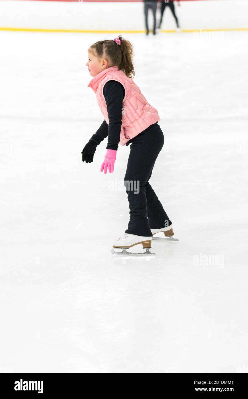 Little girl practicing figure skating elements on indoor ice skating
