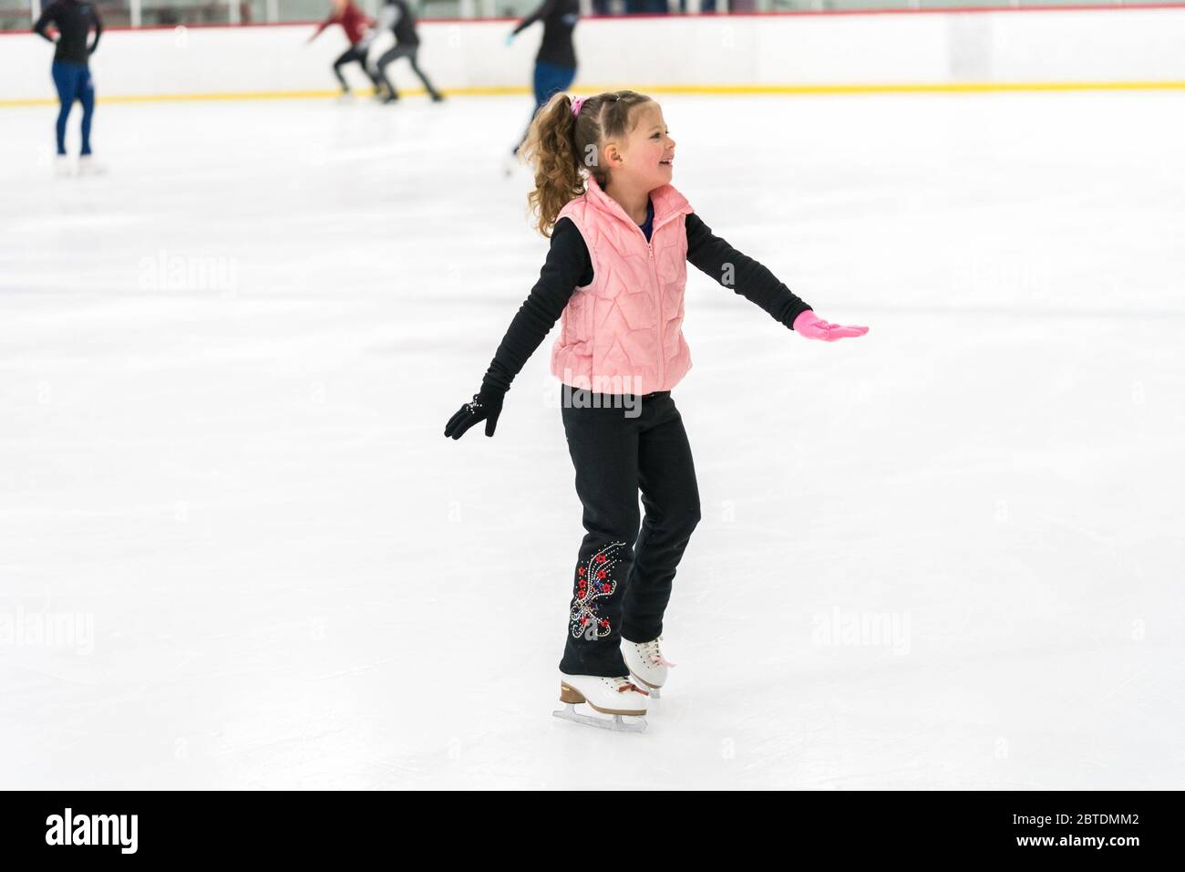 Little girl practicing figure skating elements on indoor ice skating