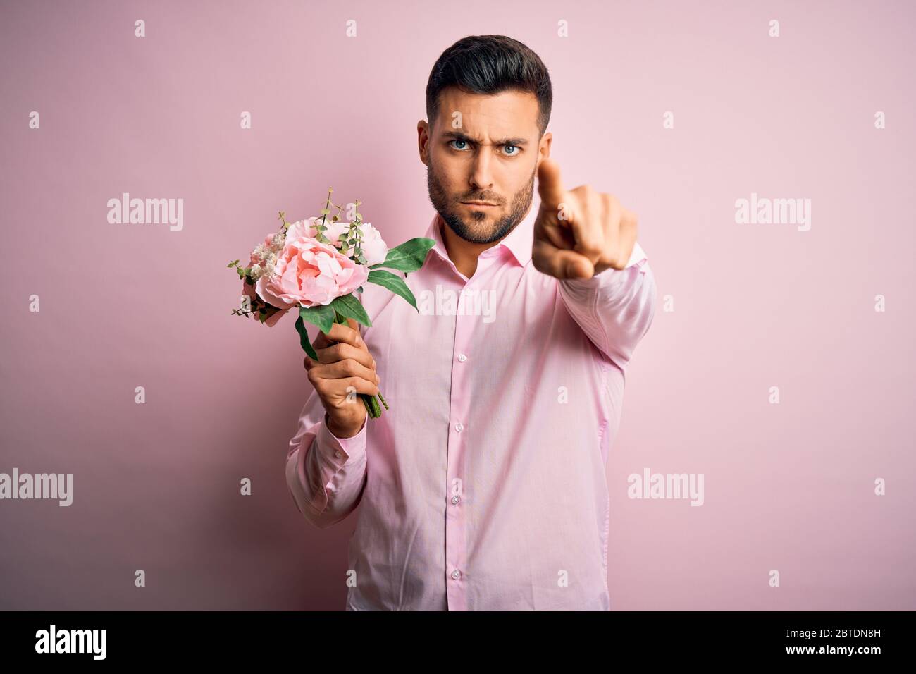 Young romatic man holding bouquet of spring flowers over pink isolatd ...
