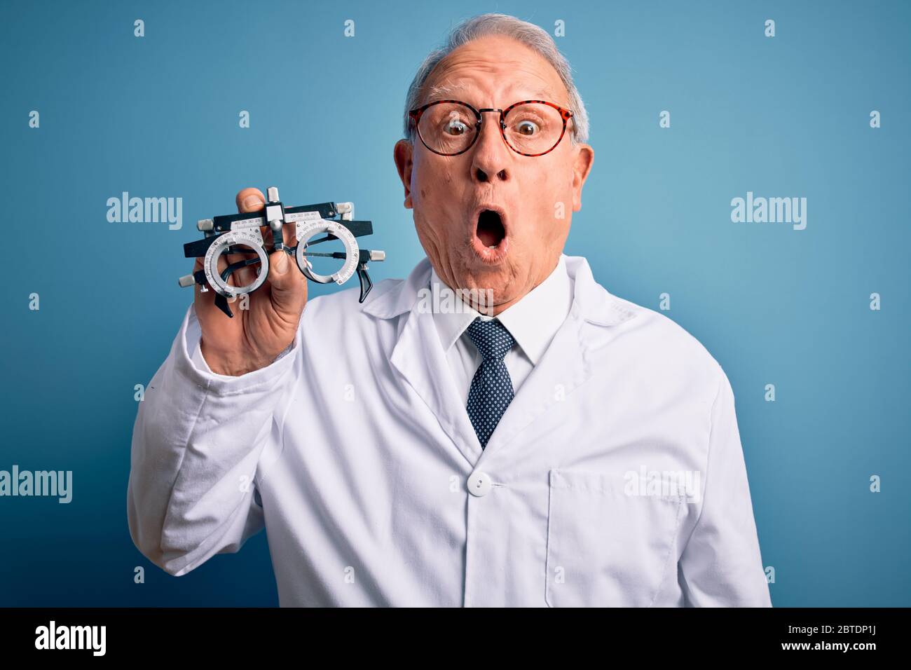 Senior grey haired optic doctor man holding optometrist eyeglasses over