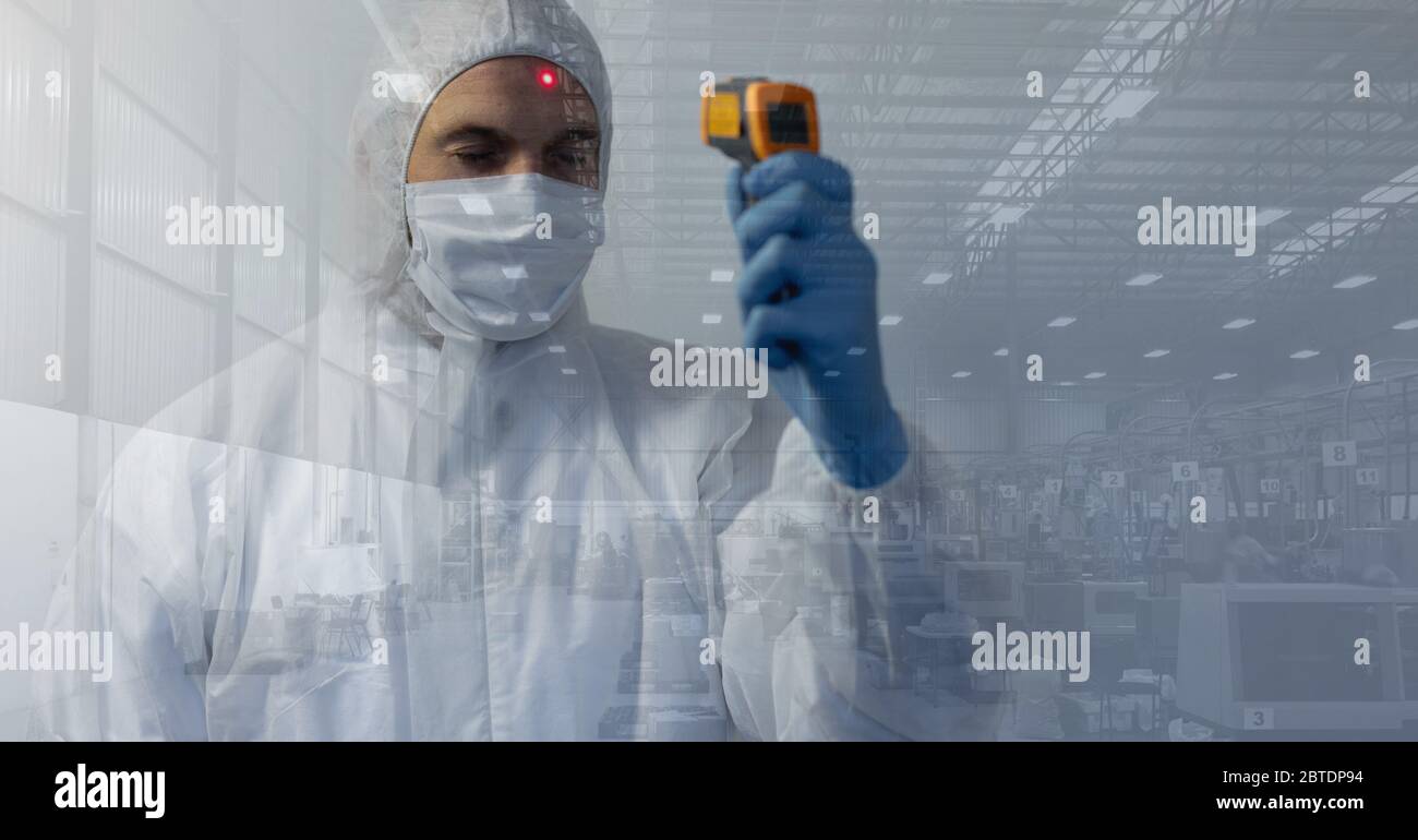 Healthcare worker wearing protective suit and using thermometer gun on himself with materials in bac Stock Photo