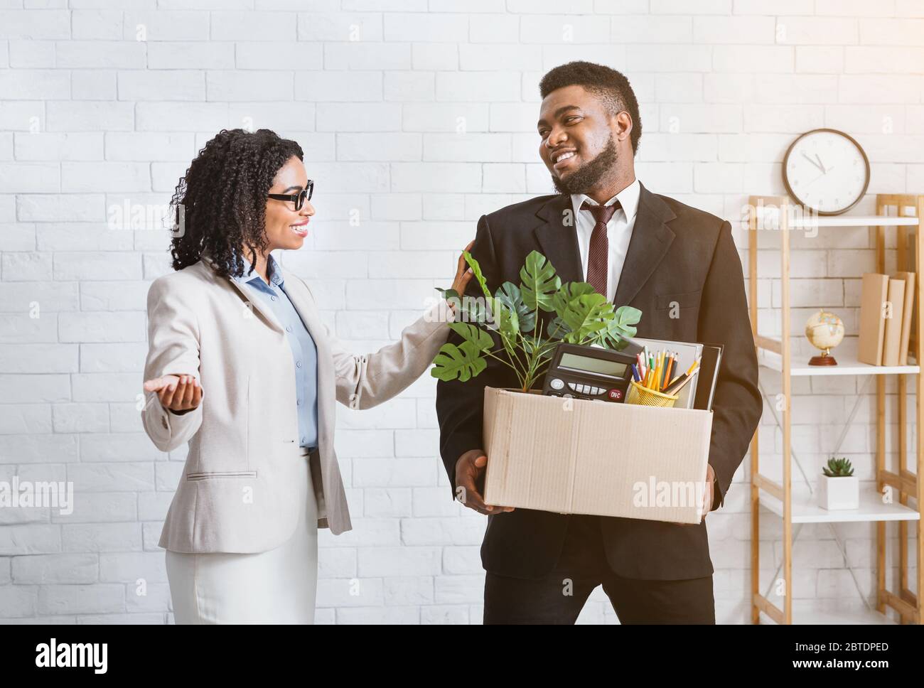 Joyful black guy with personal belongings being welcomed to work in company, meeting his new female boss Stock Photo