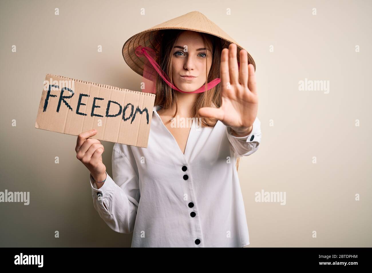Young redhead woman wearing asian traditional hat holding banner with ...