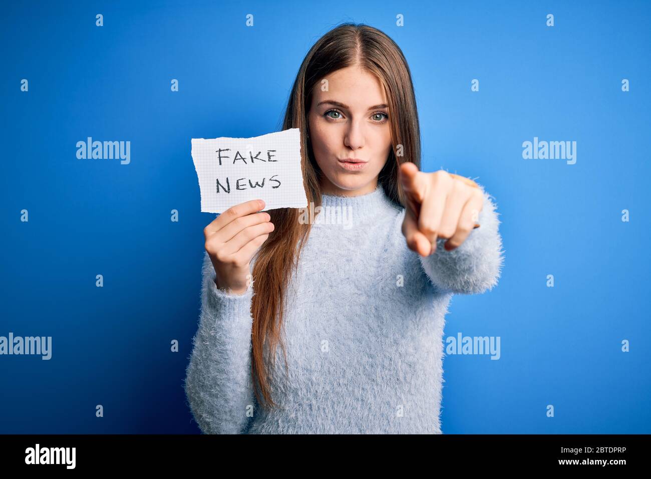Young beautiful redhead woman holding paper with fake news message over ...