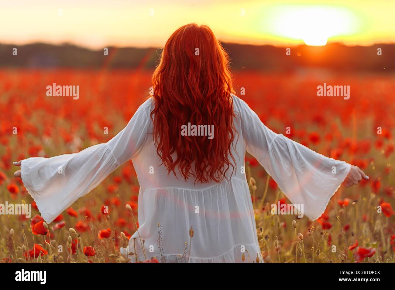Happy redhead smiling woman in white dress on field of poppies at warm ...