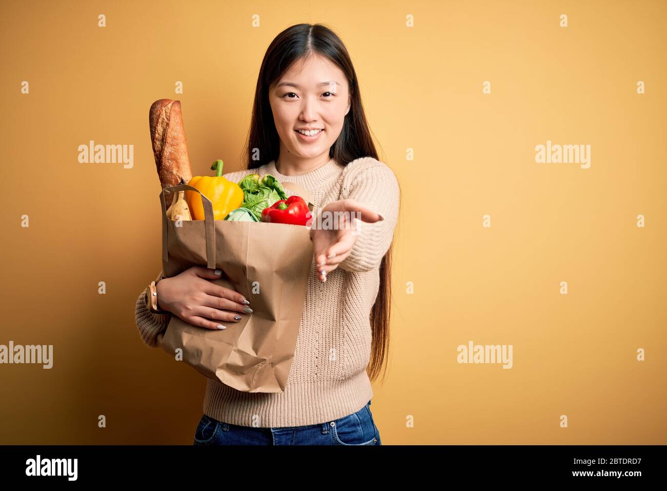 Young asian woman holding paper bag of fresh healthy groceries over