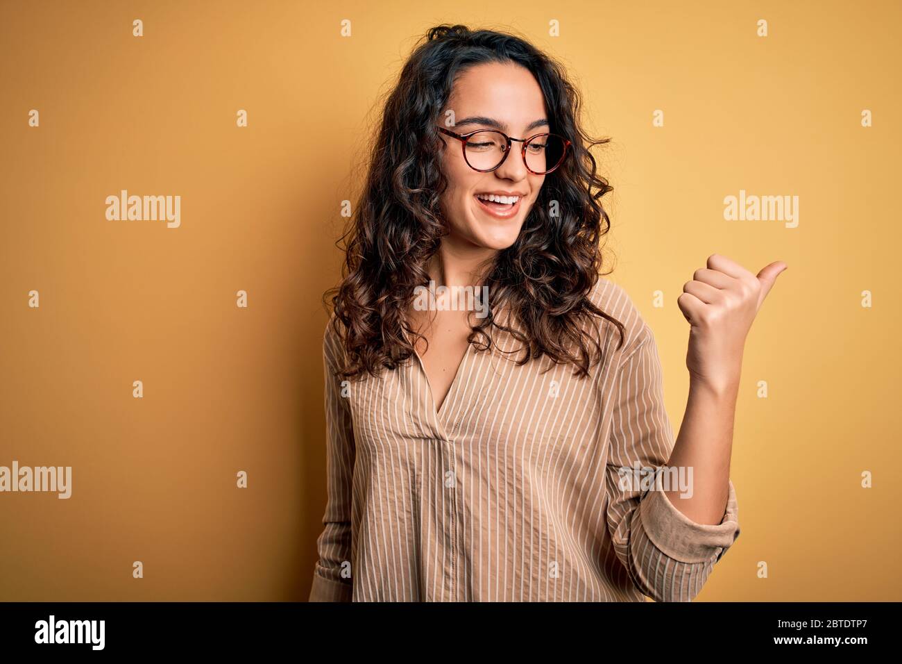Beautiful woman with curly hair wearing striped shirt and glasses over ...
