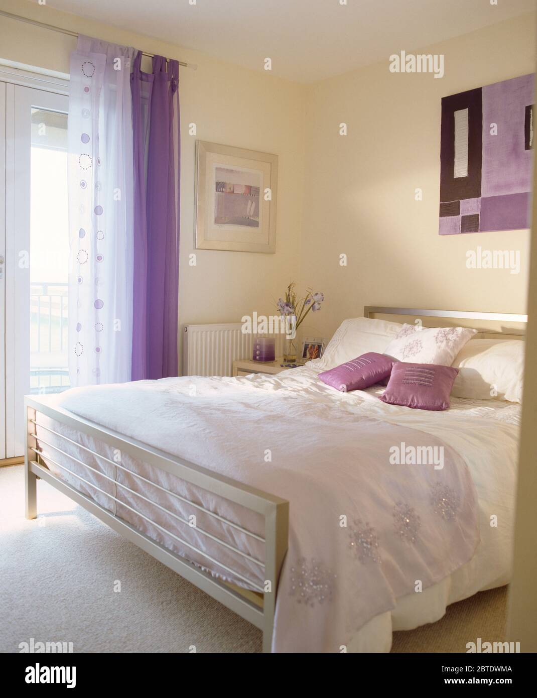 Metal bed with white linen in bedroom with mauve curtain Stock Photo
