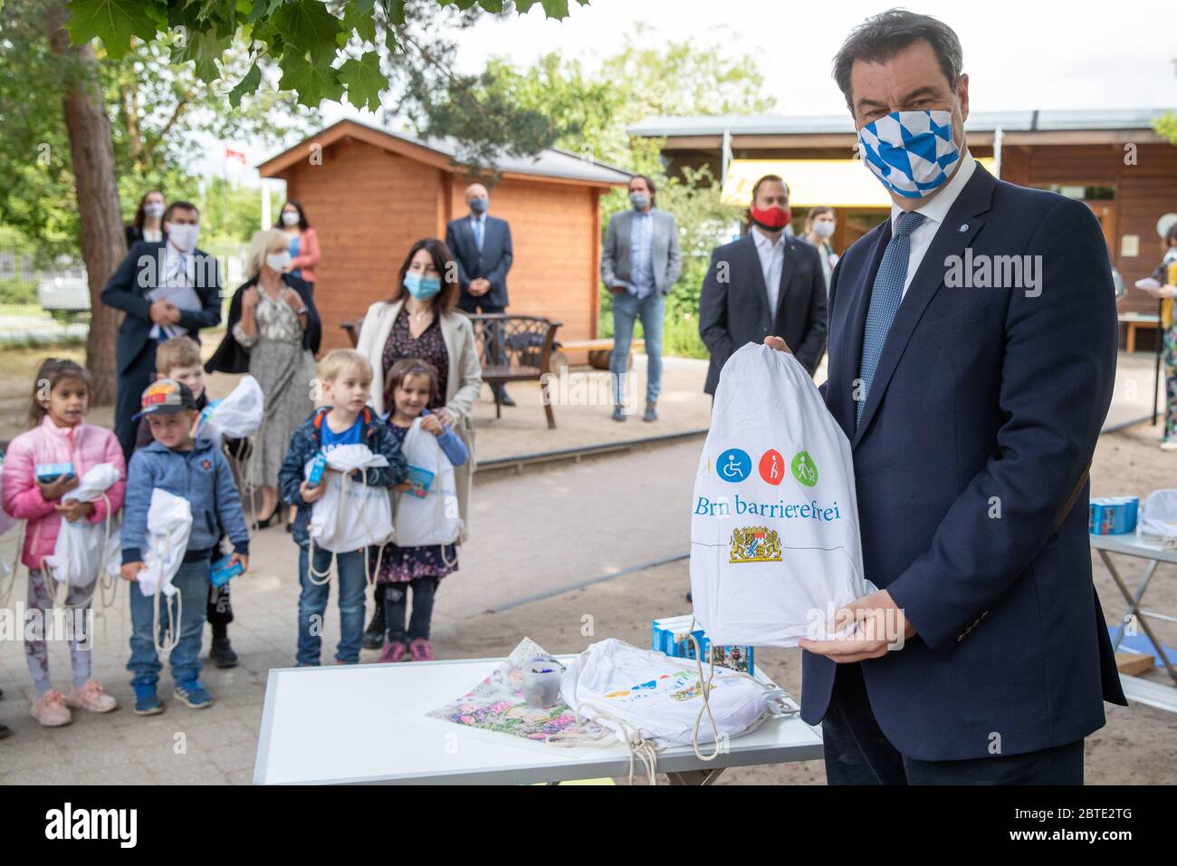 Nuremberg, Germany. 25th May, 2020. Markus Söder (CSU, r), Prime Minister of Bavaria, wears a mask during a visit to a Nuremberg kindergarten andd shows a welcome gift. Standing next to him are children, each holding such a welcome gift in their hands as they return to the kindergarten. Since 25 May, pre-school children in Bavaria have been allowed to go back to kindergarten. Credit: Daniel Karmann/dpa/Alamy Live News Stock Photo