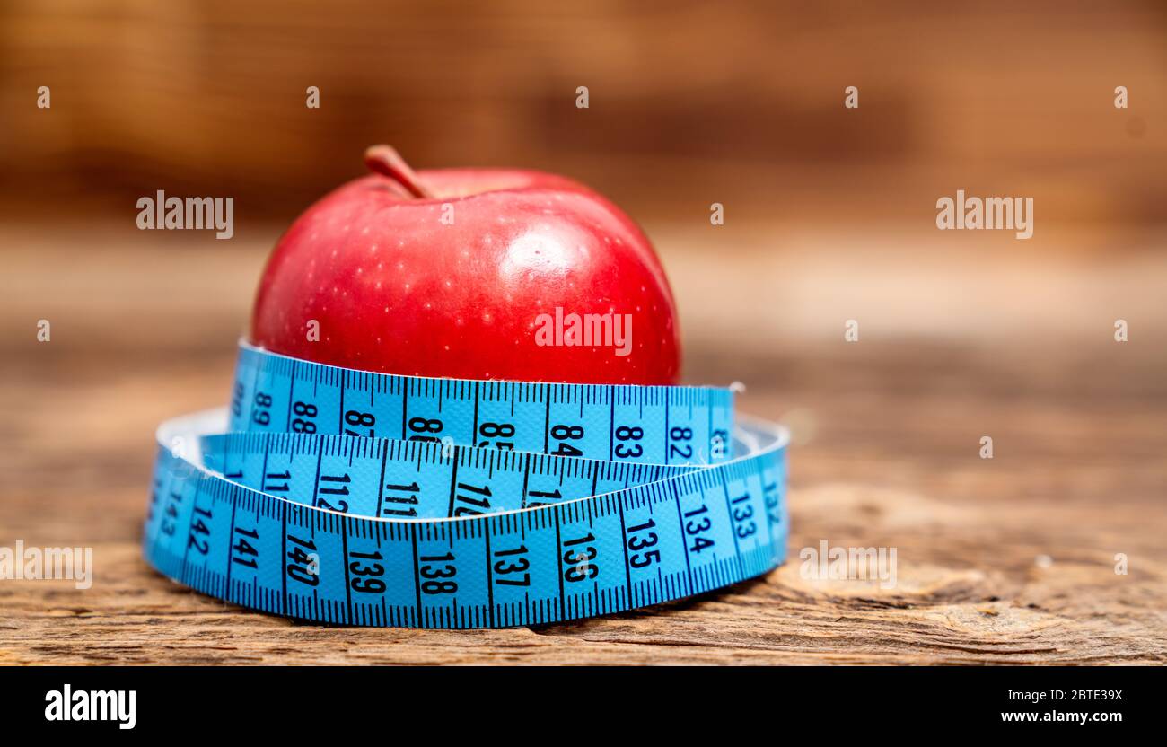 Closeup fresh red apple with measuring tape isolated on wooden background. Slim diet and eating for health Stock Photo