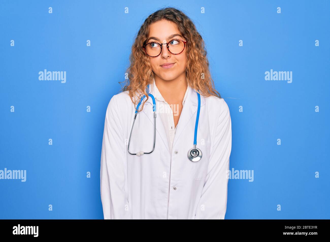 Young beautiful blonde doctor woman with blue eyes wearing coat and ...