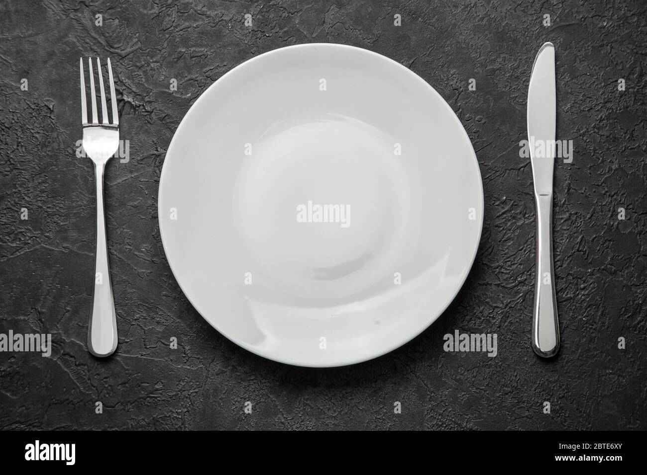 Empty white plate with knife and fork on black table Stock Photo
