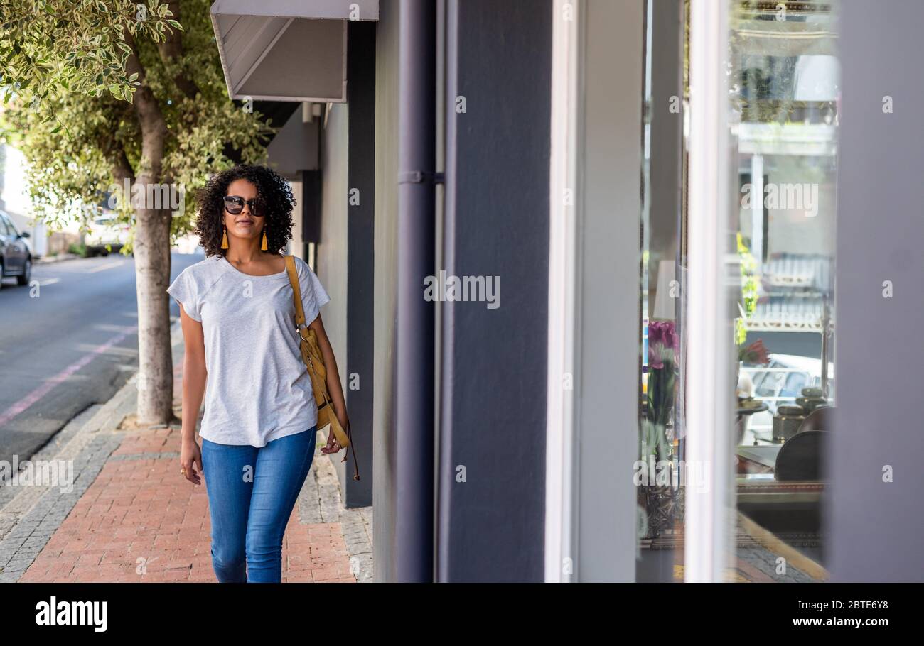 Confident young woman walking along a city sidewalk Stock Photo