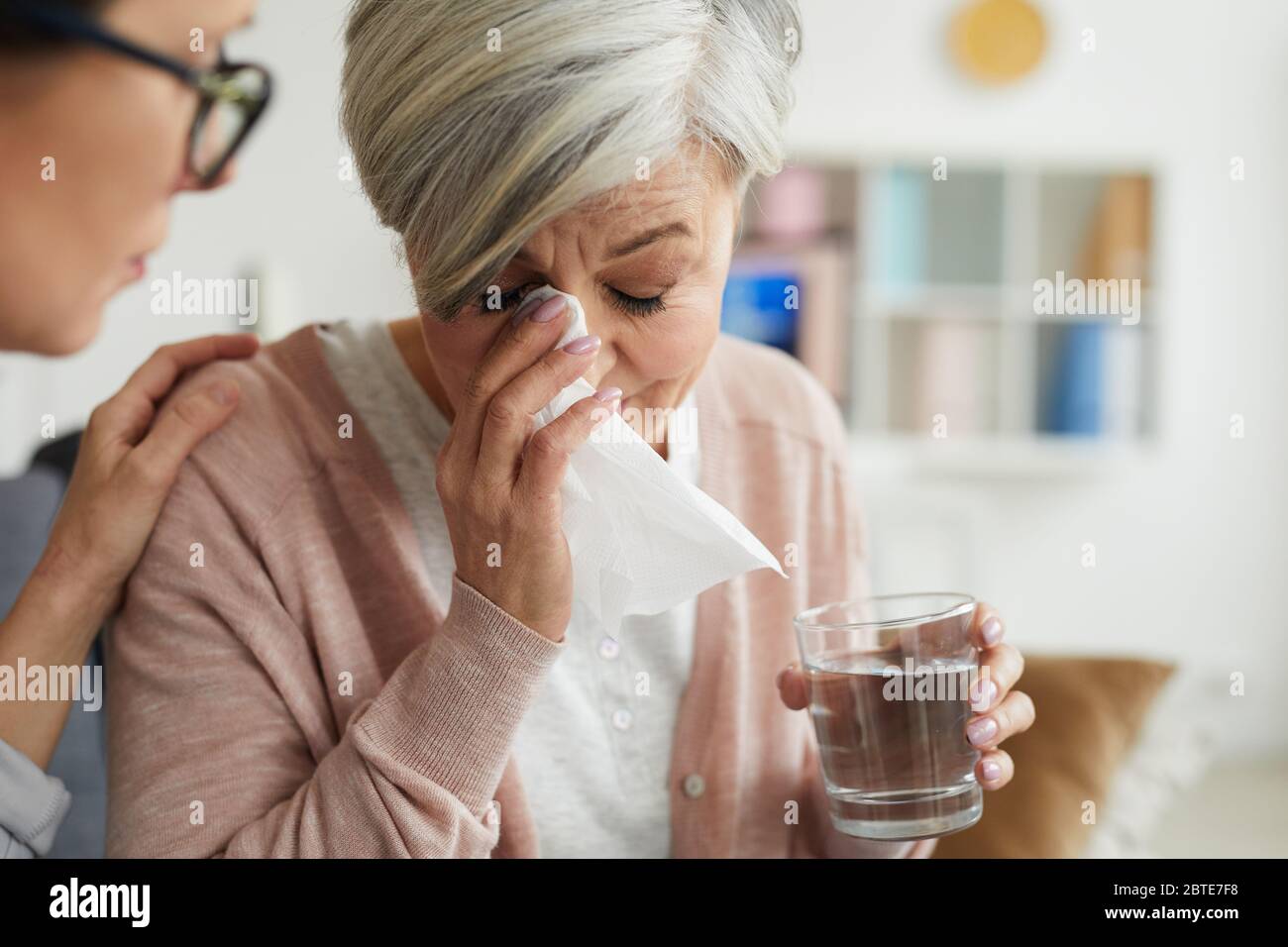 Close up portrait of elegant senior woman crying during therapy session and holding glass of water with female psychologist comforting her Stock Photo