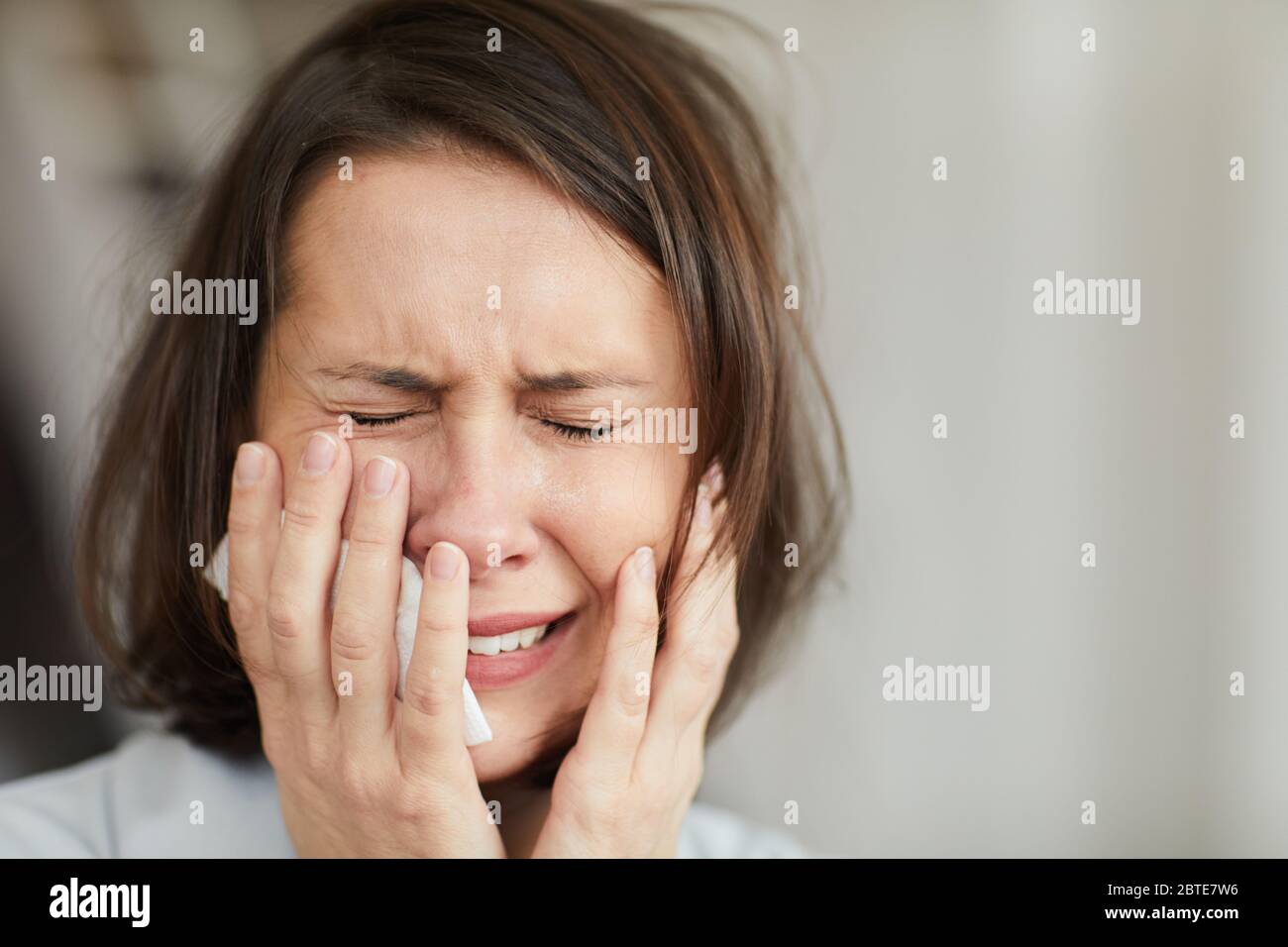 Close up portrait of disheveled adult woman crying hysterically with eyes closed and holding tissue, copy space Stock Photo