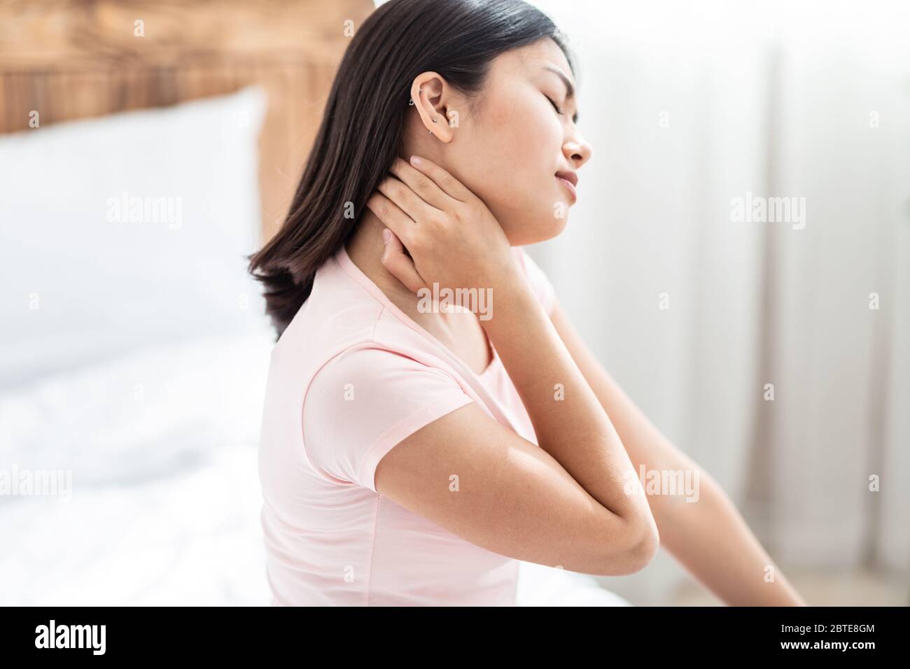 Asian Woman Massaging Aching Neck Sitting In Bed At Home Stock Photo