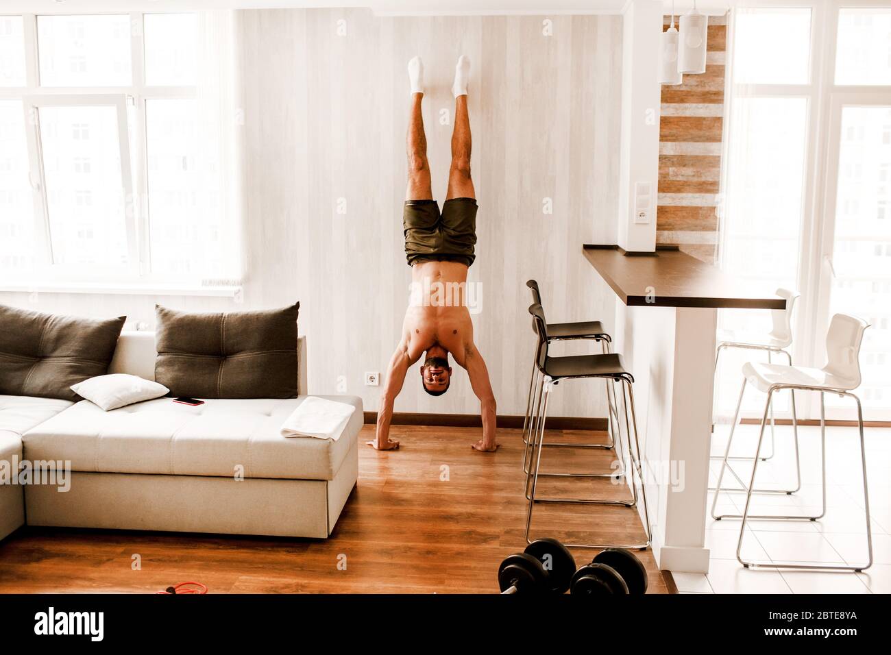 Athletic bodybuilding young man stands in his arms at home. Male