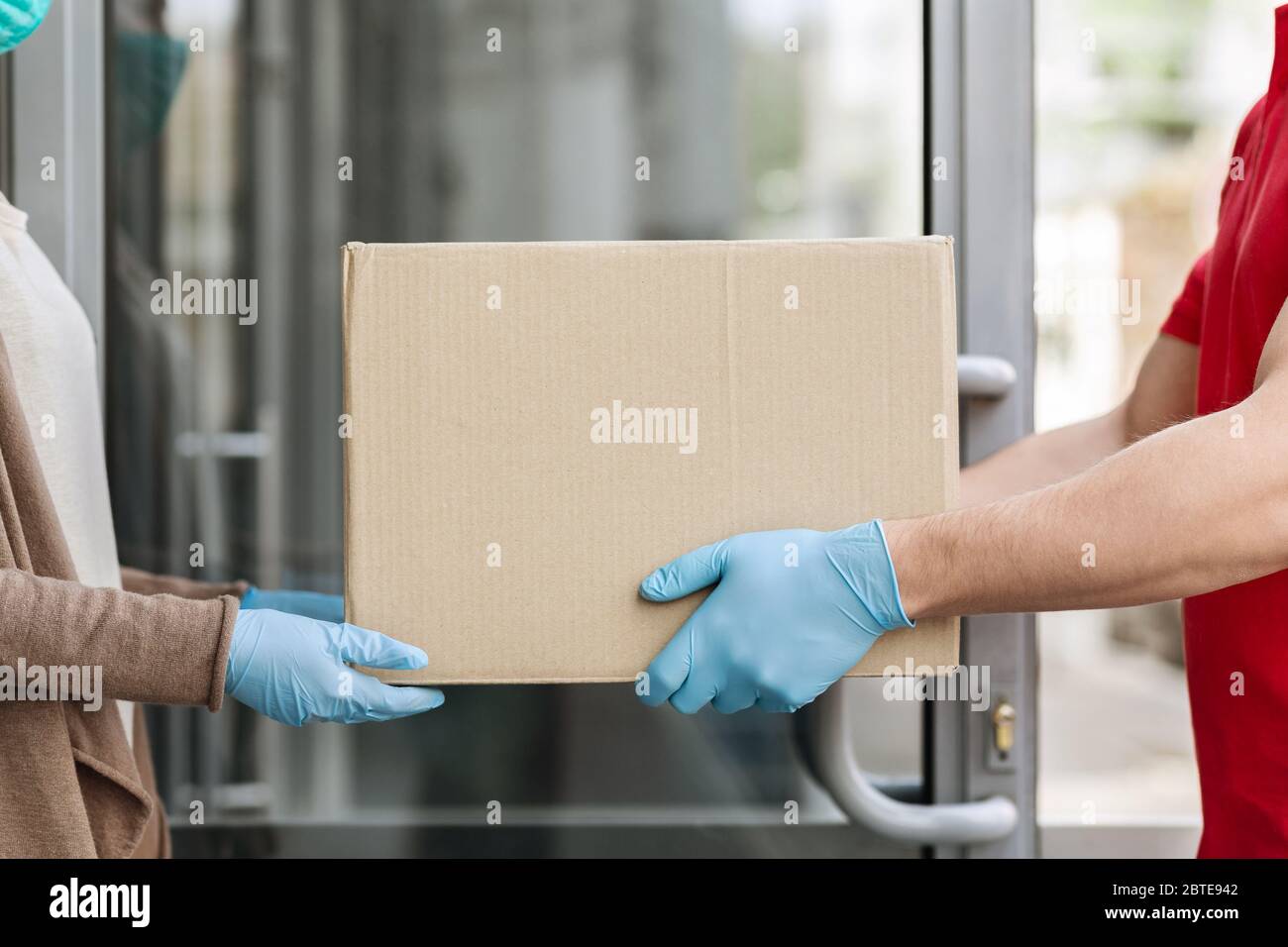 Customer care during quarantine concept. Courier in medical gloves gives box to client at door Stock Photo
