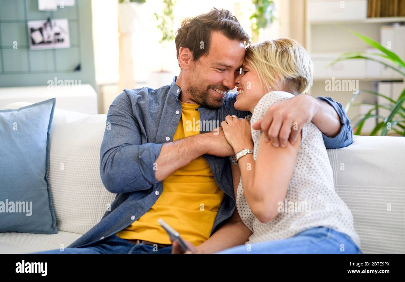 Happy couple in love sitting indoors at home, hugging. Stock Photo