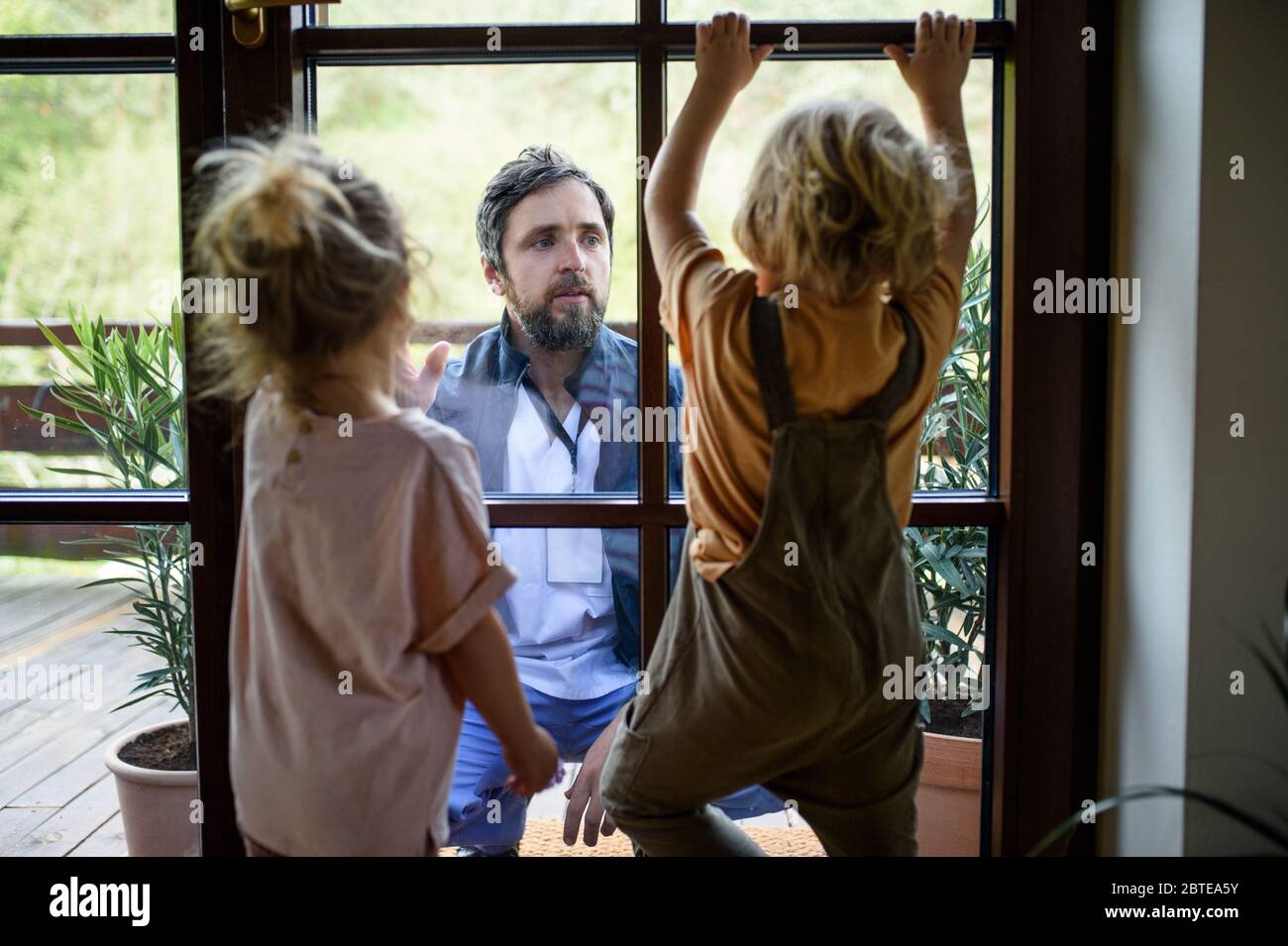 Doctor coming to see family in isolation, window glass separating them. Stock Photo