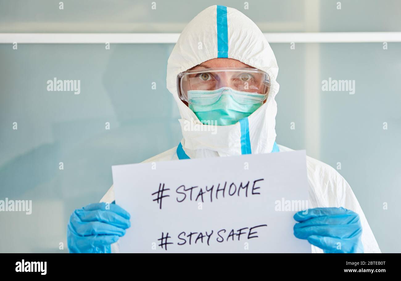 Doctor in protective clothing with #stayhome and #staysafe sign during coronavirus epidemic Stock Photo