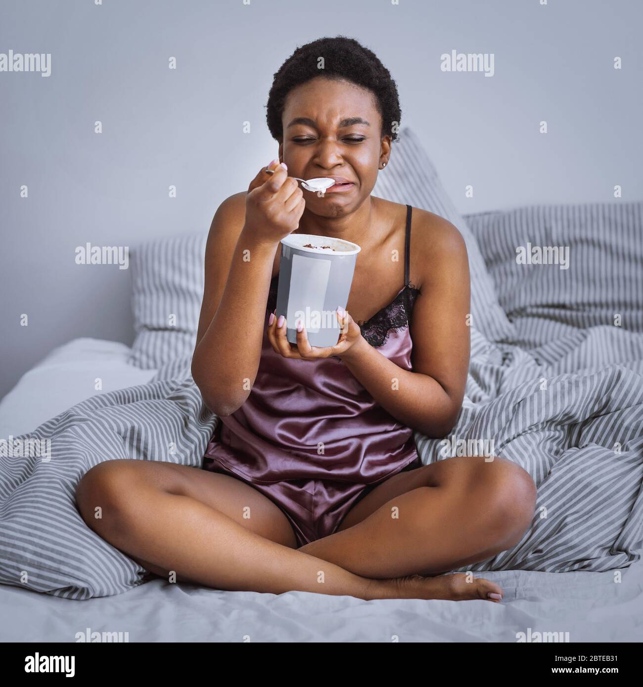 Breakup concept. Crying girl eating ice cream in bed Stock Photo