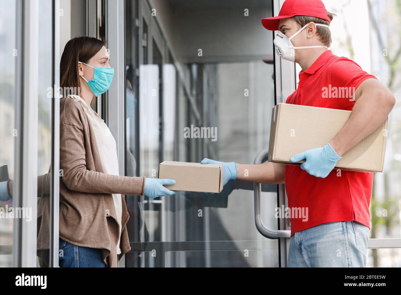 Courier in medical mask and gloves gives box to client, on porch Stock Photo