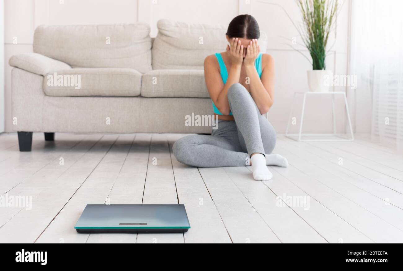 Girl Crying Sitting Near Scales Gaining Excess Weight At Home Stock Photo
