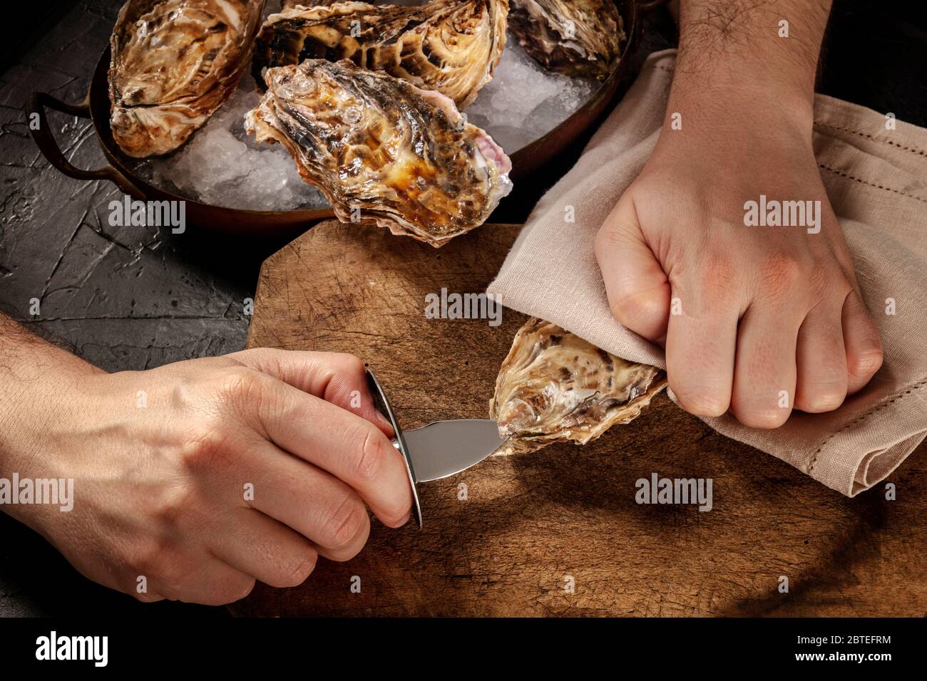 Shucking an oyster, man's hands with a special knife, opening oysters on a wooden board Stock Photo