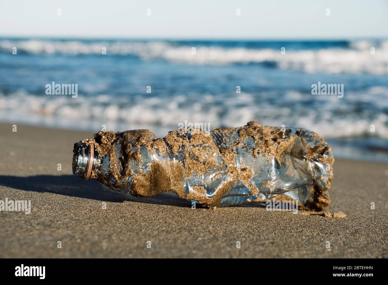 closeup of a used plastic bottle, covered with wet sand, on the sand of a lonely beach, brought back by the ocean to the seashore Stock Photo