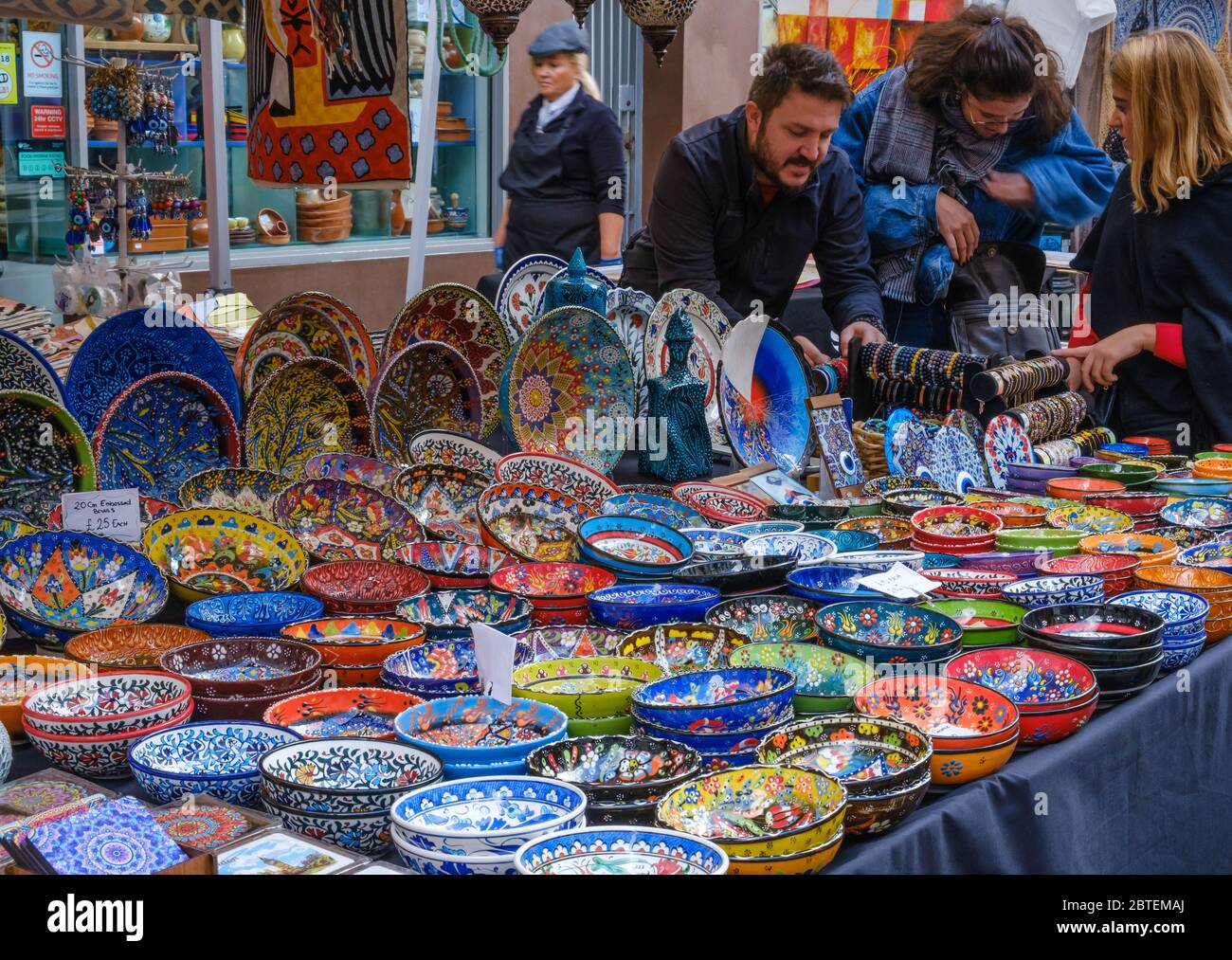 Two ladies and stall owner look at bracelets & colourful decorated