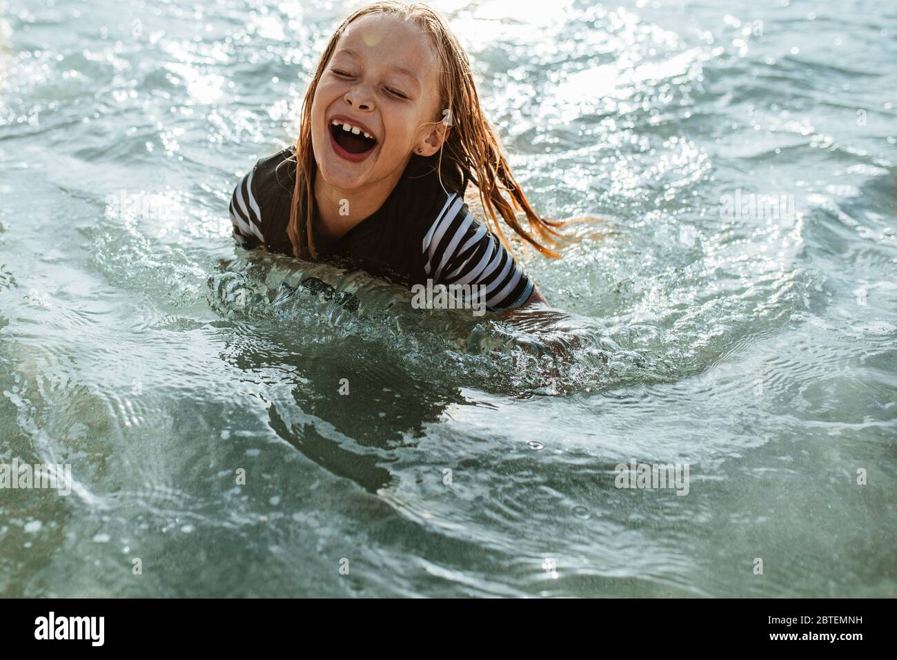 Excited girl enjoying swimming in the sea water. Young girl sitting in sea water and smiling. Stock Photo