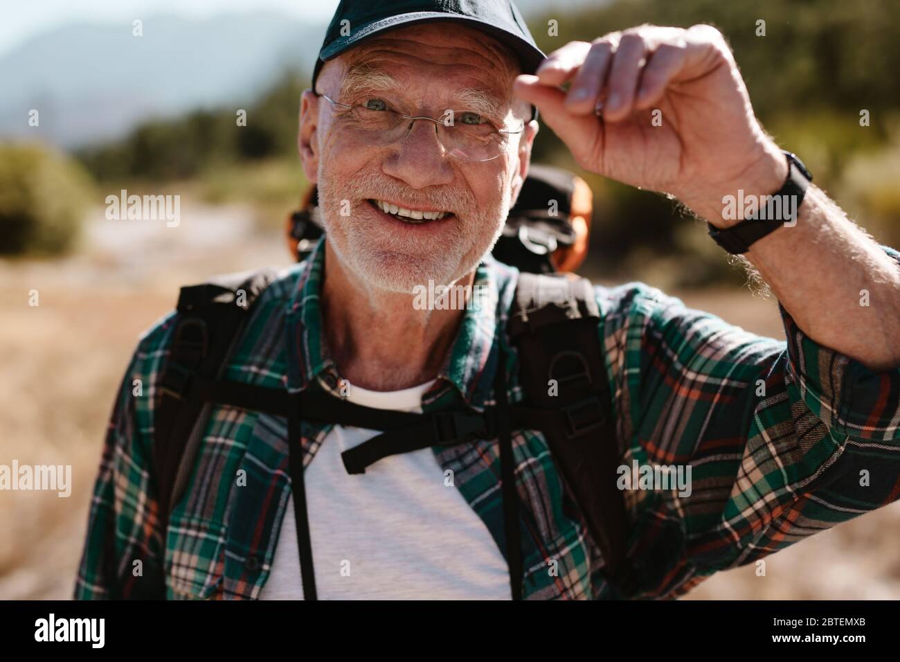 Happy senior man on hiking trip looking at camera and smiling. Fit elderly man enjoying on a hiking trip. Stock Photo