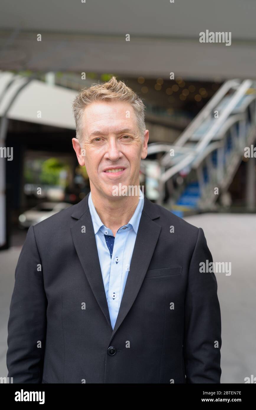 Happy mature businessman smiling at footbridge in the city Stock Photo ...