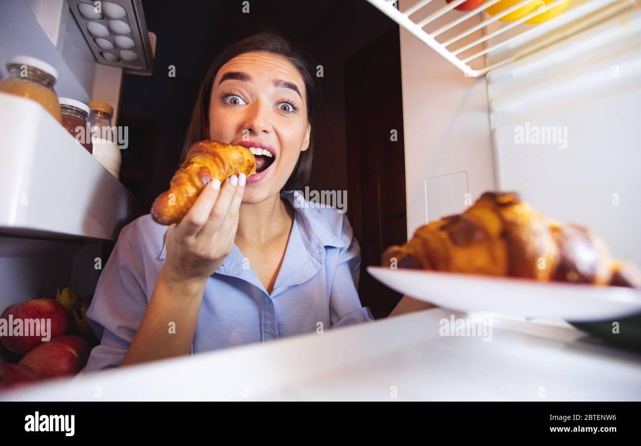 Young girl biting croissants from fridge, view from inside Stock Photo
