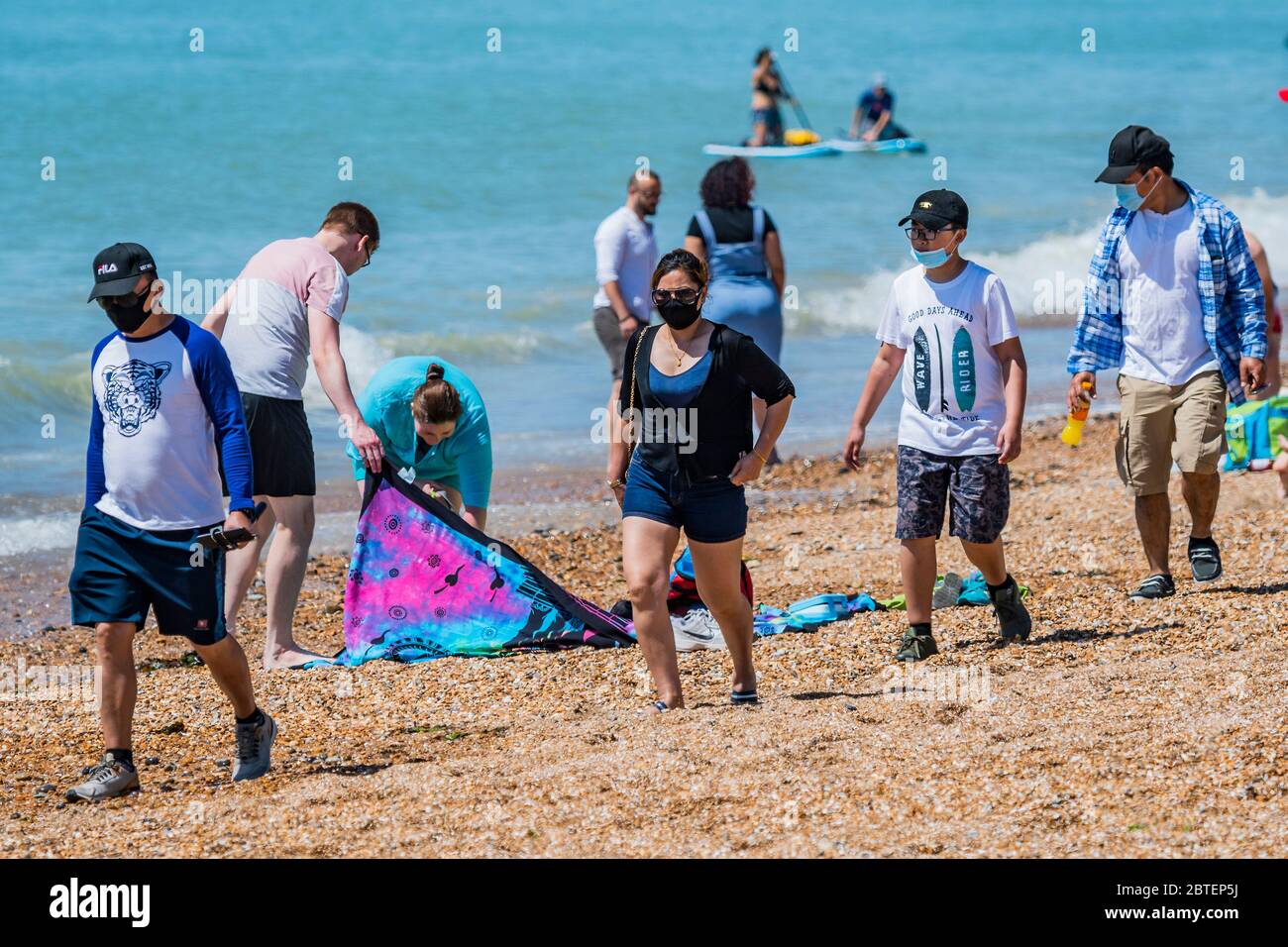 Brighton, UK. 25th May, 2020. A family in masks ar unusual on the beach - It is sunny and people come to the beach and the seaside at Brighton, during Bank holiday Monday. It is busy but still plentyu of room for social distancing. The eased 'lockdown' continues for the Coronavirus (Covid 19) outbreak. Credit: Guy Bell/Alamy Live News Stock Photo
