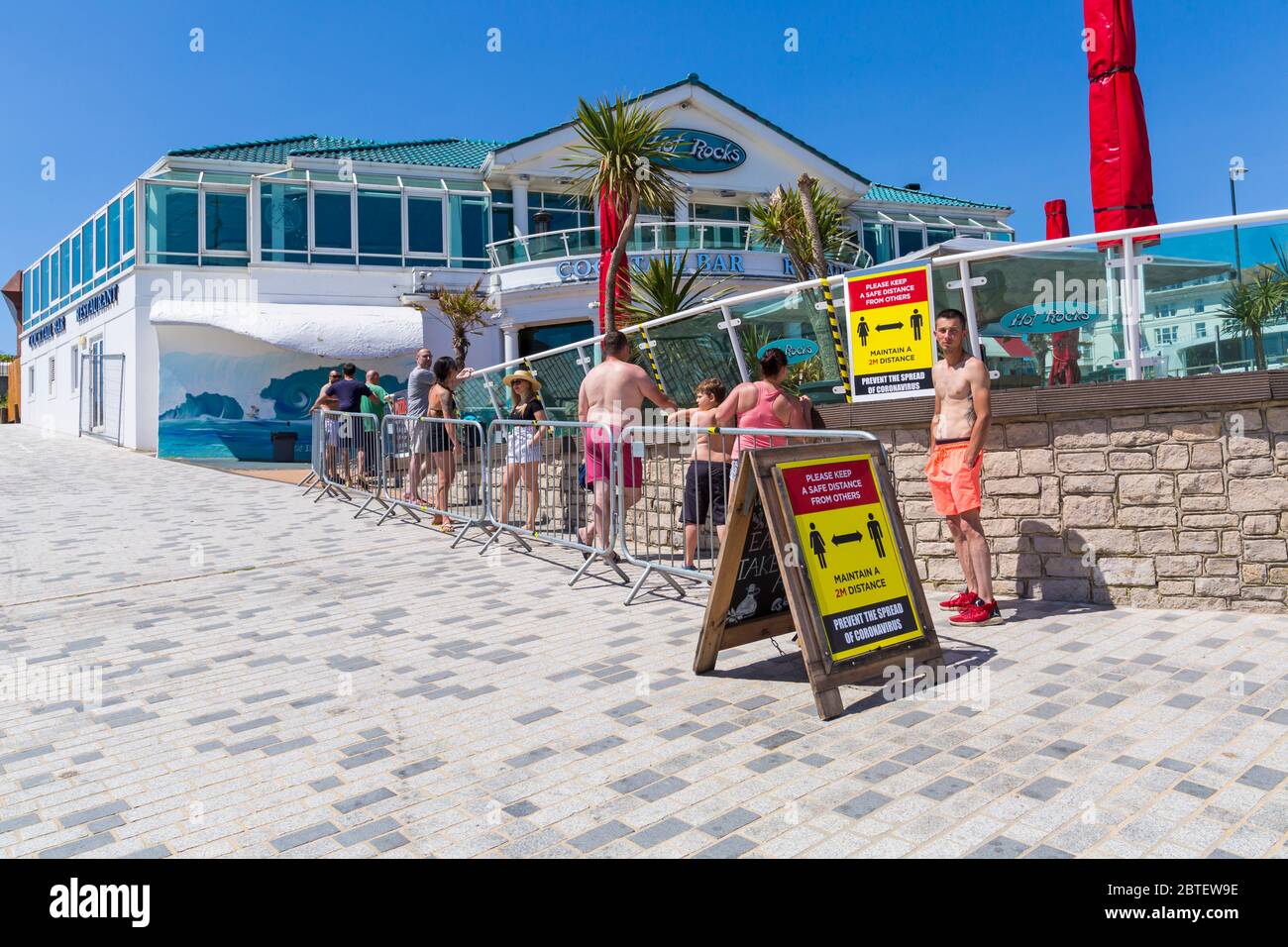 Bournemouth, Dorset UK. 25th May 2020. Social distancing as visitors queue for drinks and take away pizzas at Hot Rocks on a scorching hot day at Bournemouth beaches with clear blue skies and unbroken sunshine, as temperatures soar on Bank Holiday Monday. Sunseekers flock to the seaside and beaches are packed. Credit: Carolyn Jenkins/Alamy Live News Stock Photo